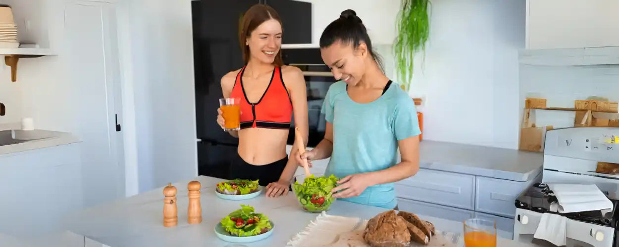 ChatGPT said:  Dua wanita sedang menyiapkan salad sehat di dapur sebagai contoh cara defisit kalori untuk pemula melalui pilihan makanan bergizi