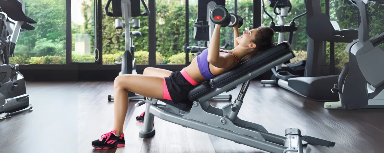 Seorang wanita sedang melakukan incline chest press di gym untuk melatih otot dada bagian atas dengan posisi tubuh miring ke atas