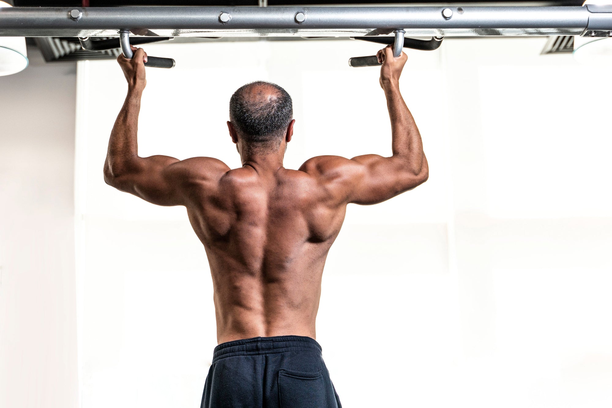 Pria bertelanjang dada melakukan pull-up di gym, menampilkan otot punggung dan lengan yang terbentuk dengan baik