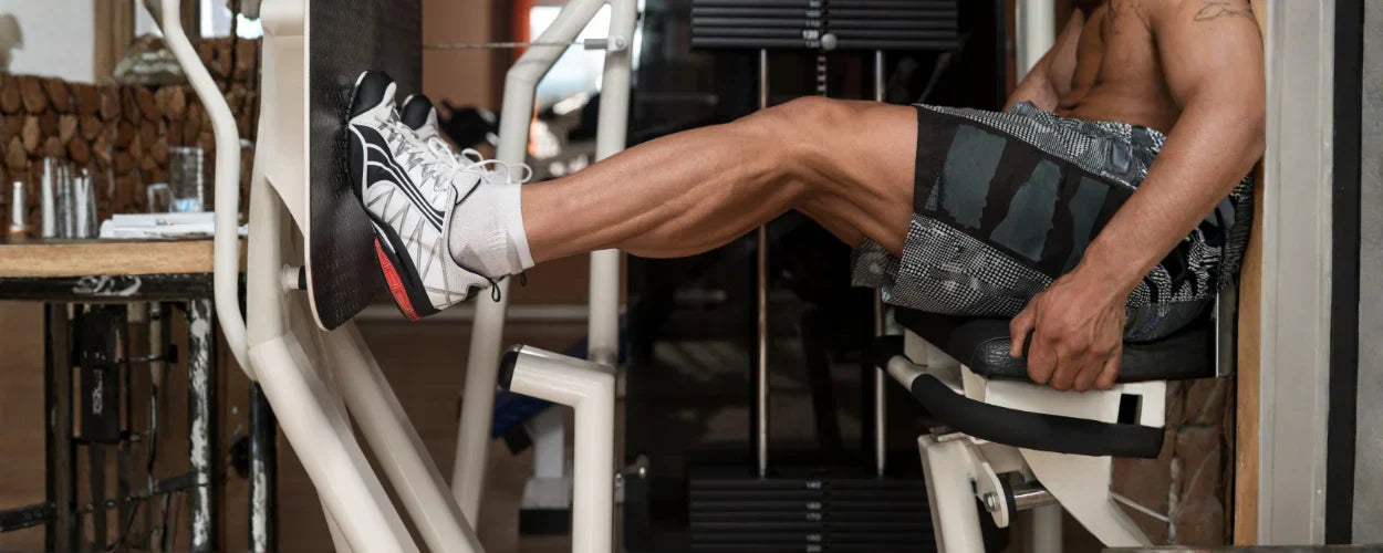 Seorang pria sedang menggunakan alat gym untuk kaki guna melatih kekuatan otot paha dan betis agar lebih kuat dan proporsional