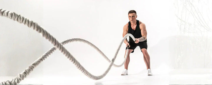 Seorang pria tengah melakukan latihan Battle Rope Cardio vs Weight Training, menunjukkan intensitas tinggi untuk meningkatkan kekuatan dan daya tahan tubuh