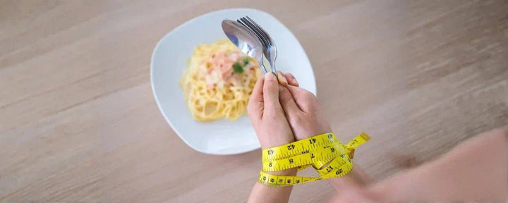 Seseorang dengan tangan terikat pita garis meteran di depan sepiring makanan menggambarkan pentingnya cara cutting yang benar agar diet tetap sehat dan seimbang.