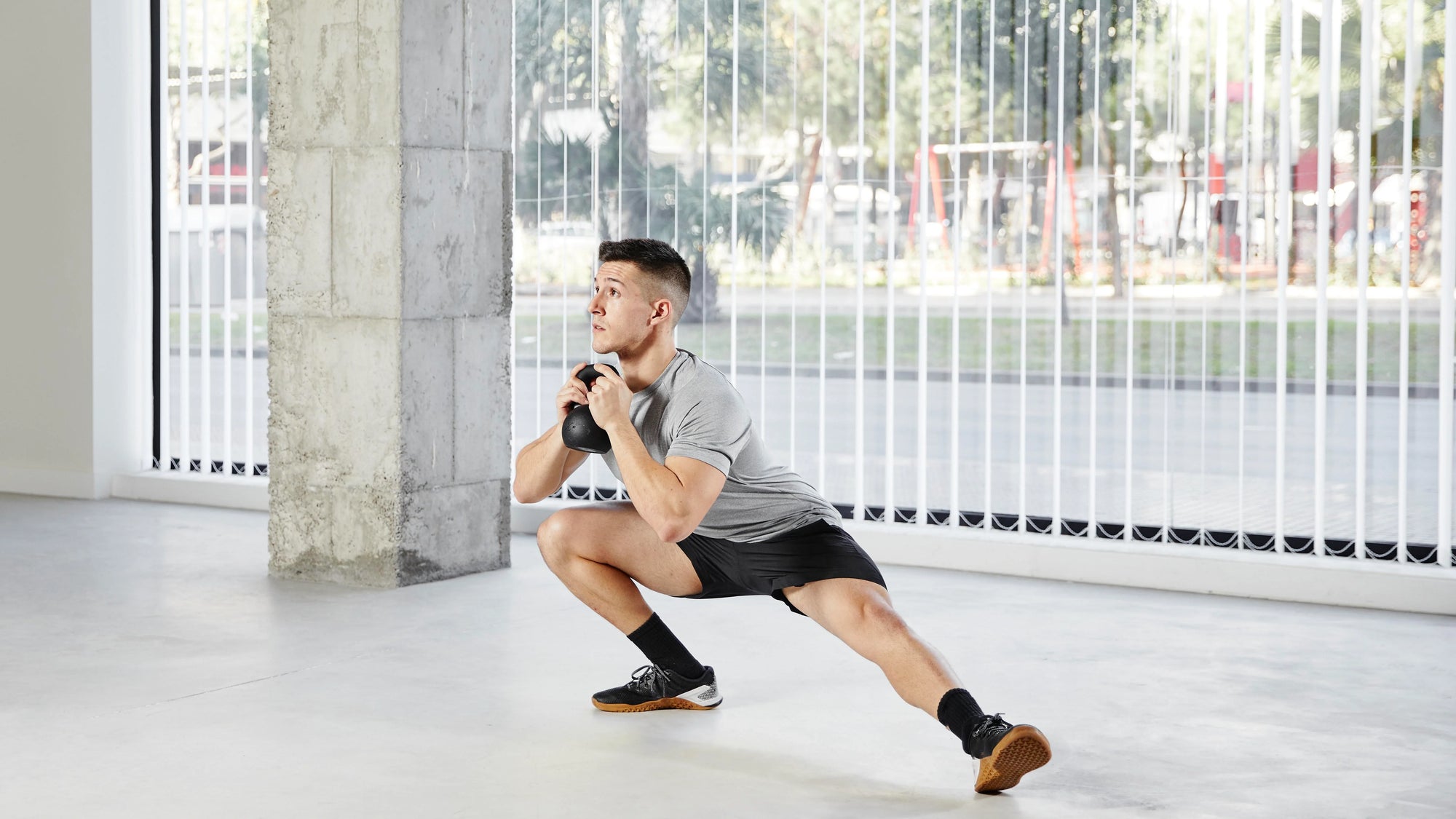 Seorang pria melakukan latihan lunges dengan kettlebell di rumah, menjadi contoh praktis cara dan contoh latihan kekuatan.