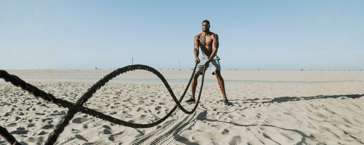 seorang pria sedang mempraktikkan cara menggunakan battle rope dengan teknik gelombang ganda untuk melatih kekuatan dan daya tahan otot tubuh