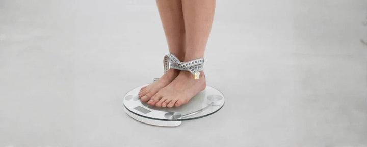 Seorang individu berdiri di atas timbangan dengan pita ukur di pergelangan kaki, menggambarkan konsep cara menghitung BMI untuk memantau kesehatan tubuh