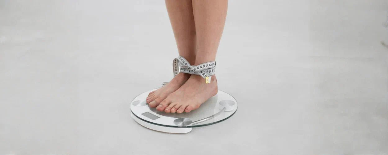 Seorang individu berdiri di atas timbangan dengan pita ukur di pergelangan kaki, menggambarkan konsep cara menghitung BMI untuk memantau kesehatan tubuh