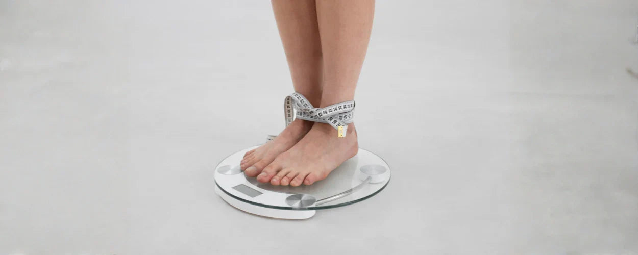 Seorang individu berdiri di atas timbangan dengan pita ukur di pergelangan kaki, menggambarkan konsep cara menghitung BMI untuk memantau kesehatan tubuh