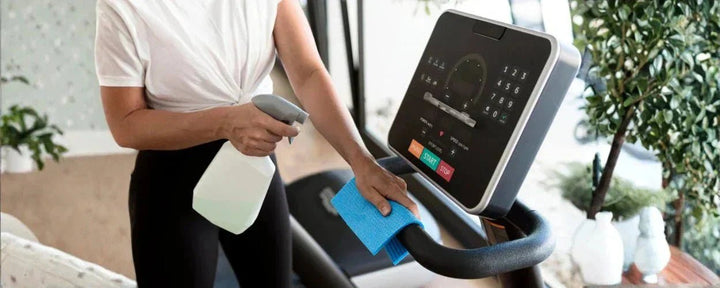 seseorang sedang membersihkan panel treadmill menggunakan cairan pembersih dan kain microfiber sebagai bagian dari cara merawat treadmill agar tetap awet dan higienis