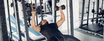 seorang pria berbaju hitam sedang mengangkat 2 dumbbell di gym sebagai upaya latihan dumbbell bench press