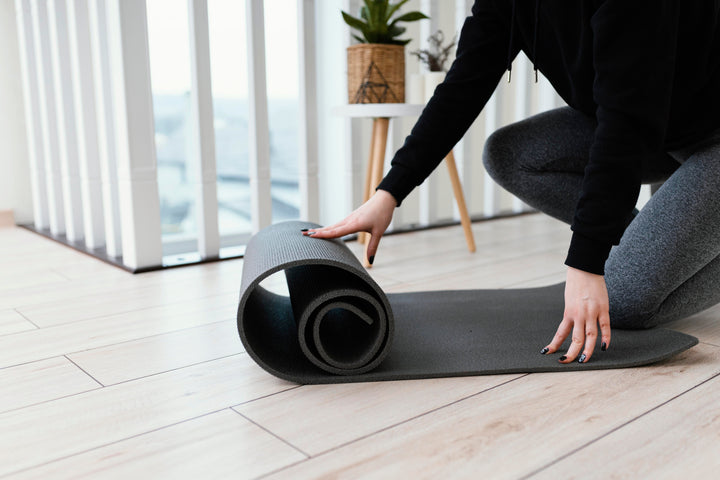 Perempuan sedang menggelar matras yoga di ruang tamu sebelum memulai latihan di rumah.