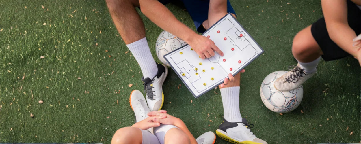 seorang pelatih yang menjelaskan formasi sepakbola kepada pemain menggunakan papan taktik di lapangan.