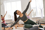 Wanita sedang melakukan latihan Pilates di atas Wunda Chair bersama peserta lainnya di studio dengan cahaya alami.