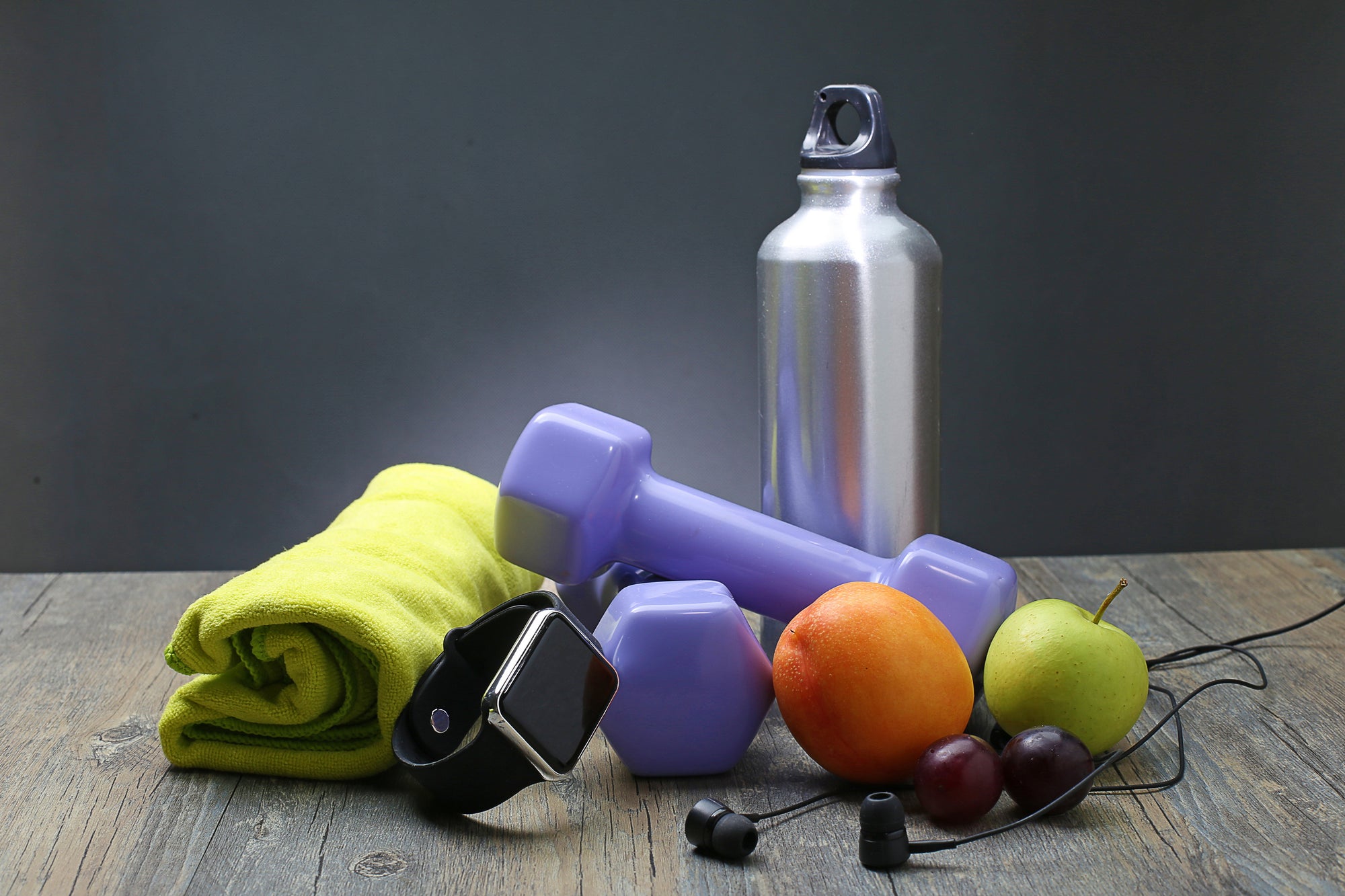 seperangkat aksesoris olahraga yang terdiri dari botol minum, handuk, jam tangan, barbel, earphone, hingga buah-buahan