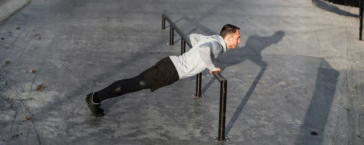 Pria sedang melakukan incline push up menggunakan palang besi di area outdoor untuk melatih kekuatan dada dan lengan