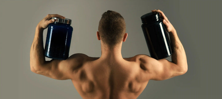 seorang pria berotot yang memegang dua wadah suplemen besar, menggambarkan fokus pada kandungan whey protein yang bermanfaat untuk membangun dan memulihkan massa otot