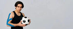 Seorang atlet memegang bola dengan serius sambil menggunakan kinesio tape sepak bola berwarna biru di lengan kanannya