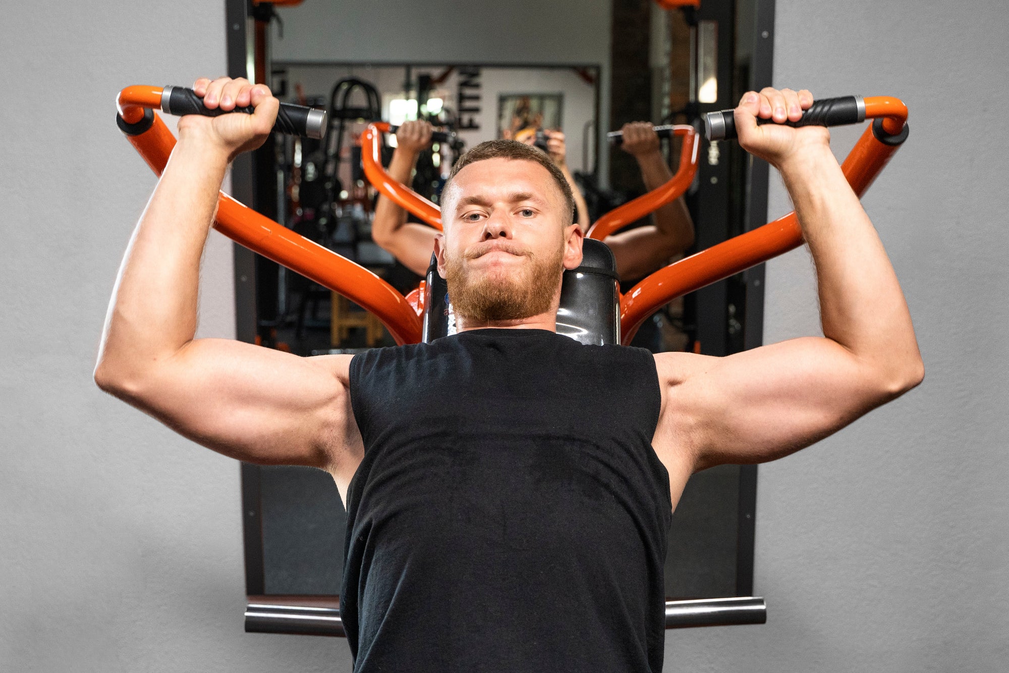 Pria sedang melakukan shoulder press menggunakan mesin gym untuk melatih otot bahu bagian depan dan samping