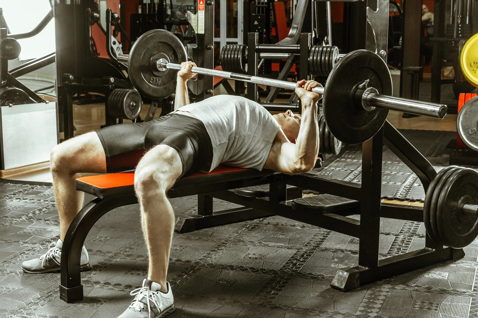 Pria melakukan latihan bench press dengan barbel di gym untuk melatih otot dada dan trisep