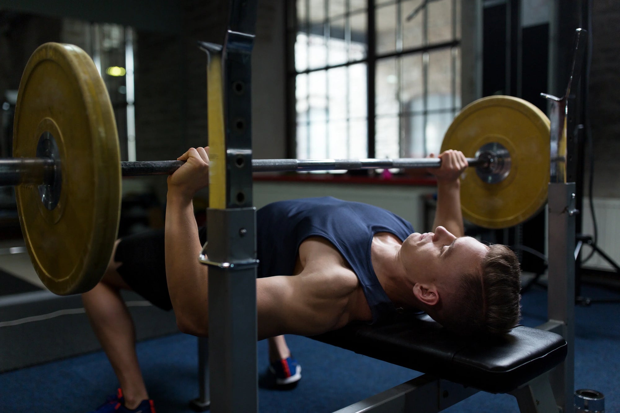 Seorang pria melakukan latihan bench press dengan barbel di gym menggunakan rak bench press datar.