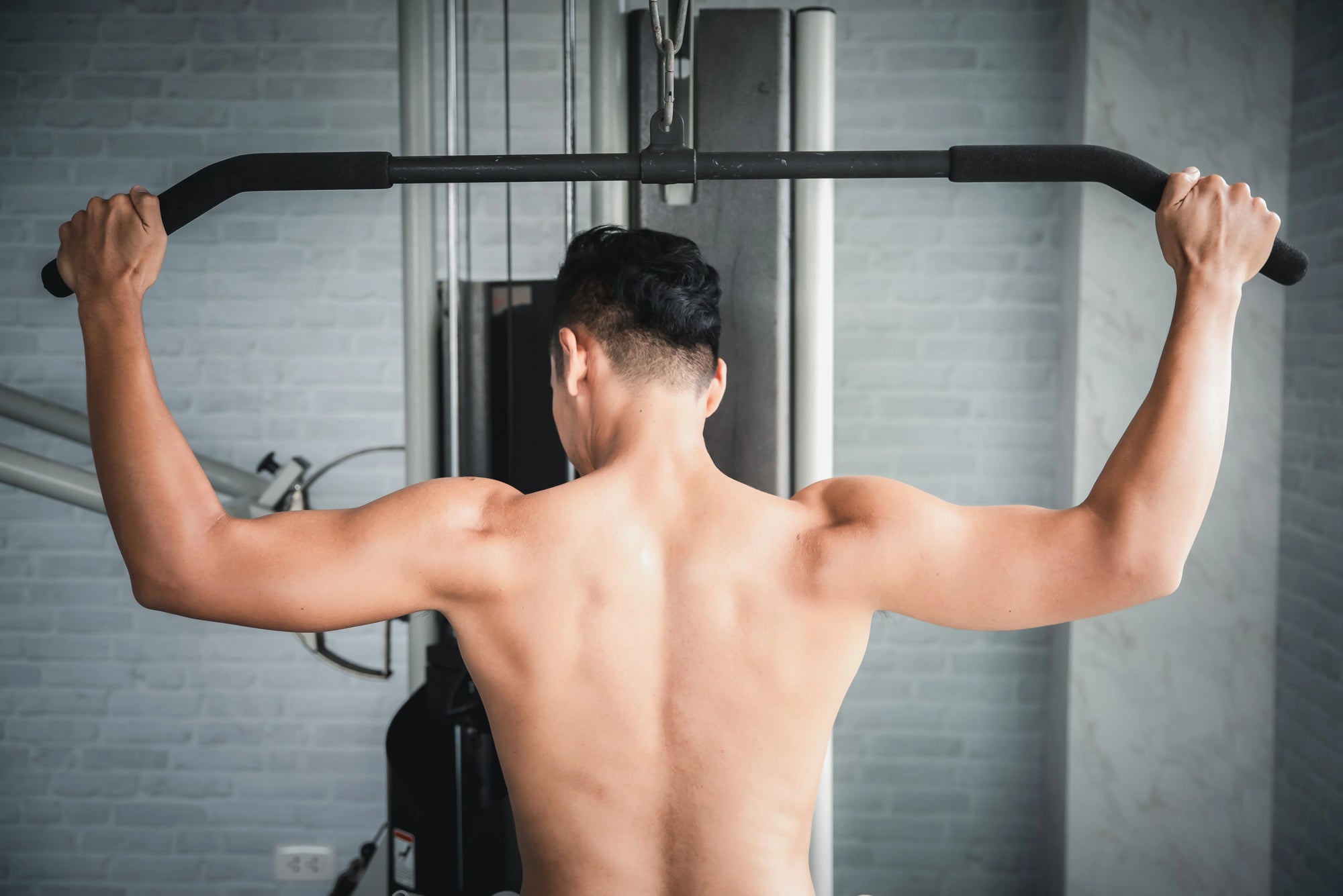 Seorang pria sedang melakukan latihan otot bahu menggunakan mesin kabel di gym untuk memperkuat dan membentuk bahu.