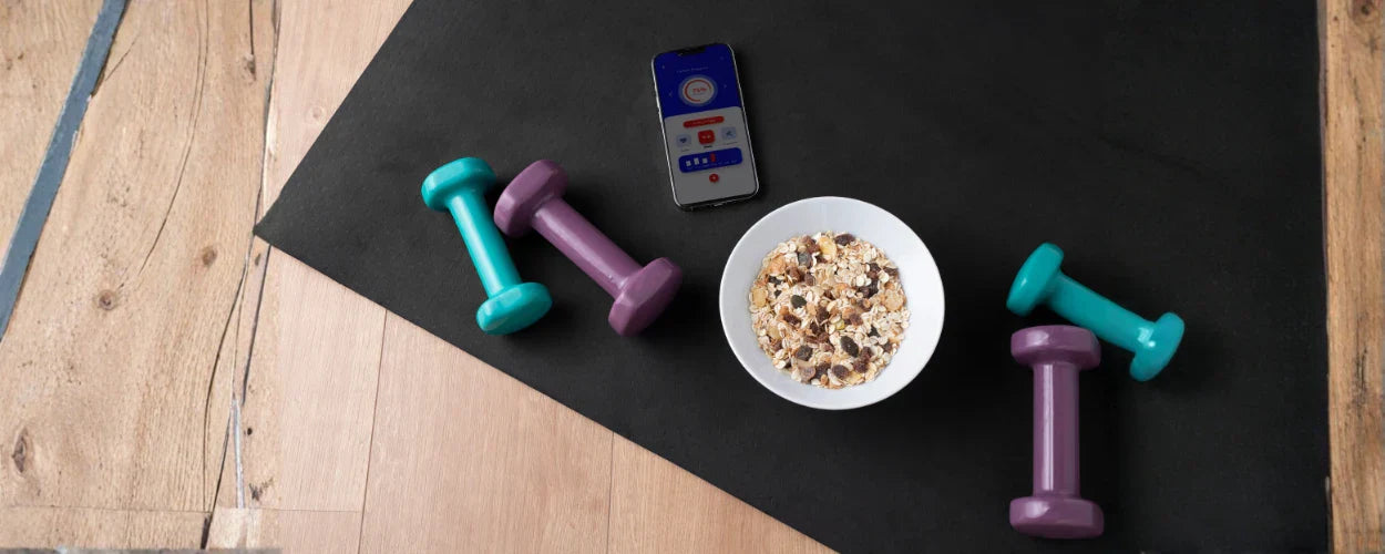 semangkuk oatmeal dengan dumbbell dan ponsel di sekitarnya, menggambarkan contoh makanan pre workout yang sehat untuk mendukung energi sebelum latihan