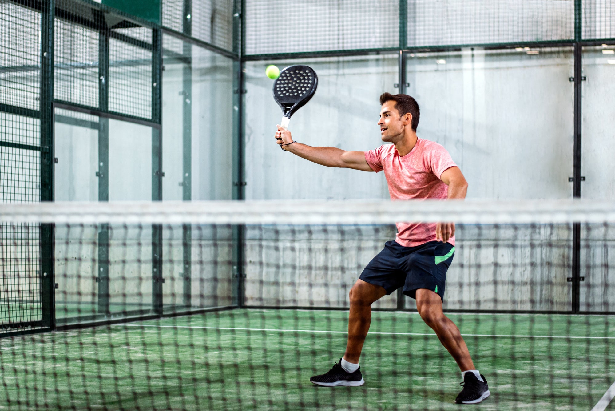 Olahraga padel pria di lapangan indoor, menggunakan raket padel dan sepatu olahraga hitam