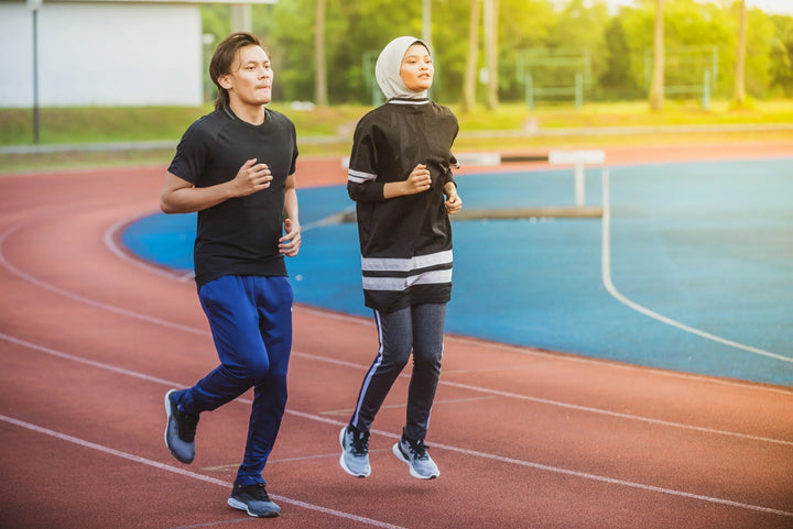 sepasang orang yang sedang jogging di lintasan atletik, menggambarkan manfaat olahraga lari untuk menjaga kebugaran tubuh dan kesehatan jantung