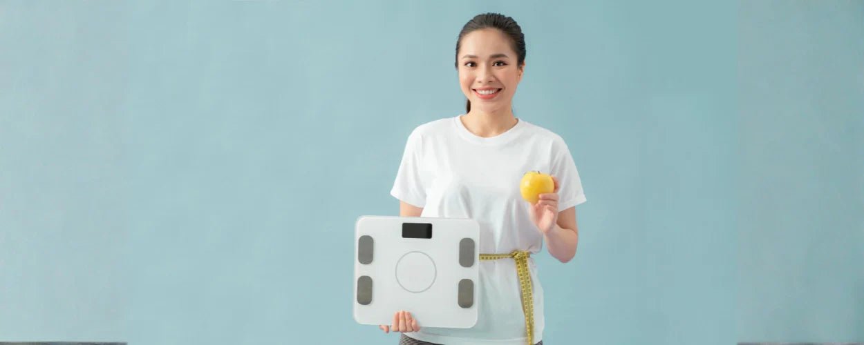 seorang wanita tersenyum sambil memegang timbangan dan apel sebagai simbol pentingnya menjaga berat badan ideal melalui pola hidup sehat