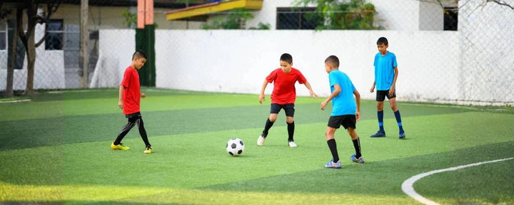 Beberapa anak bermain bola di lapangan rumput kecil, menggambarkan suasana pertandingan santai yang relevan dengan perbandingan mini soccer vs futsal