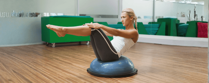 seorang wanita melakukan olahraga dengan balance ball di rumah untuk melatih keseimbangan tubuh dan kekuatan otot inti
