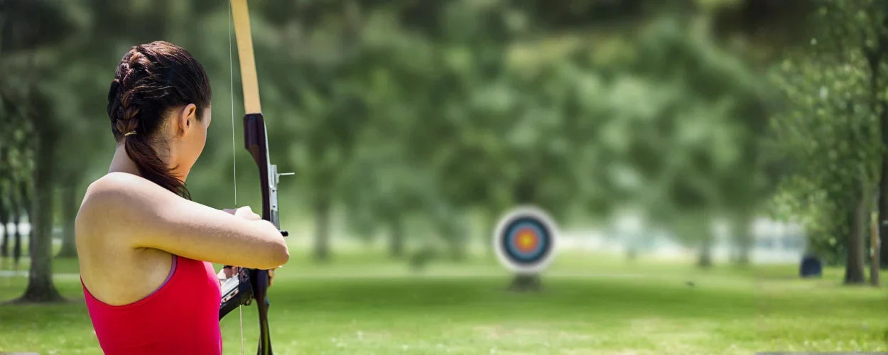seorang wanita sedang memegang busur ke arah papan panah sebagai bentuk olahraga panahan