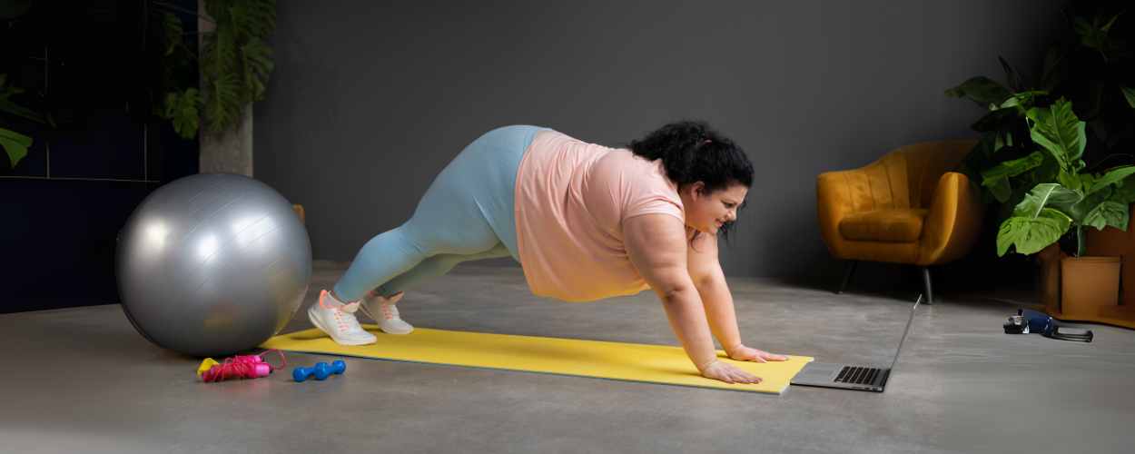 Seorang wanita sedang melakukan plank di atas matras dengan panduan laptop sebagai contoh olahraga yang cepat membakar lemak di rumah