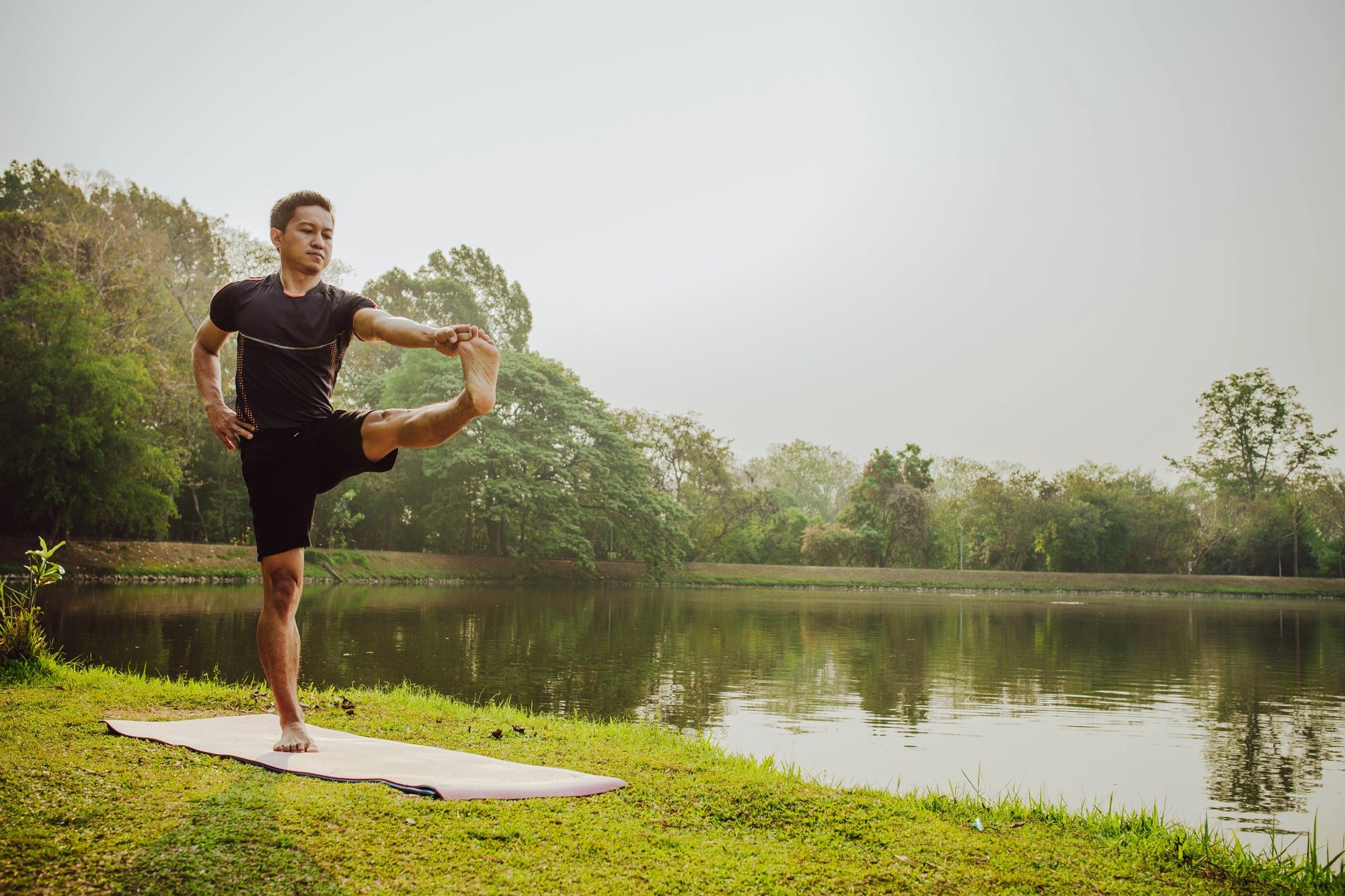 seorang pria melakukan yoga di tepi danau, contoh olahraga yang melatih keseimbangan serta konsentrasi tubuh