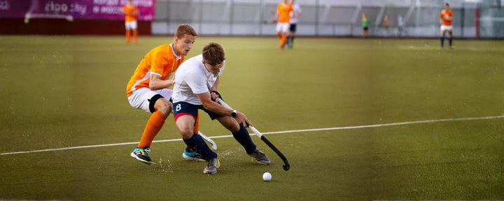 Permainan hockey terlihat menuntut kecepatan dan kontrol stik yang baik, di mana pemain berusaha menggiring bola sambil menghindari tekanan ketat dari lawan
