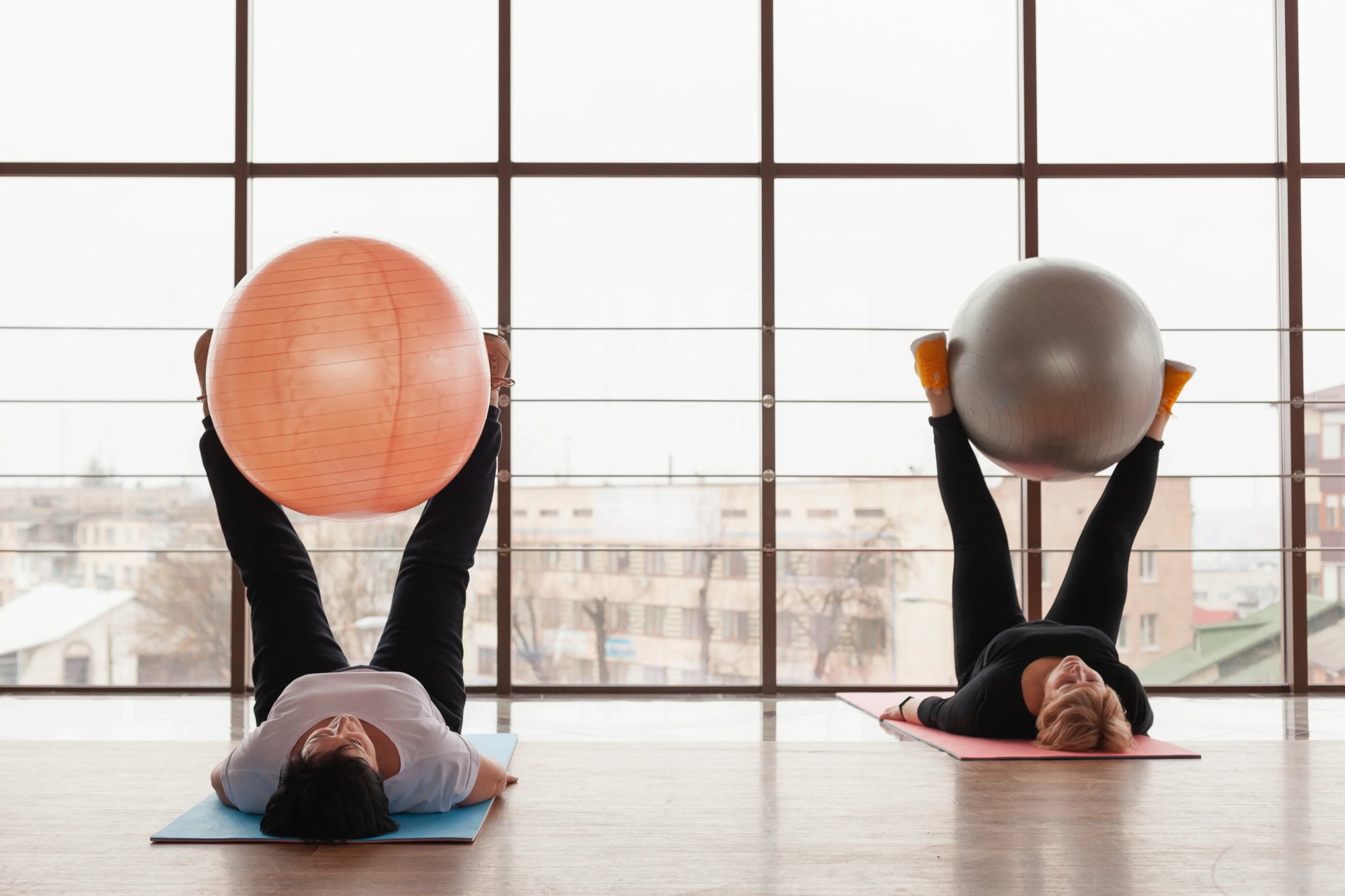 Dua orang sedang berlatih dengan gym ball di studio, memperlihatkan perbedaan fokus latihan pilates vs kalistenik dalam membangun kekuatan dan keseimbangan tubuh.