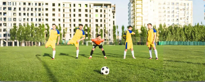 sekelompok pemain yang bersiap di lapangan, menggambarkan posisi pemain sepak bola saat mengatur formasi sebelum tendangan