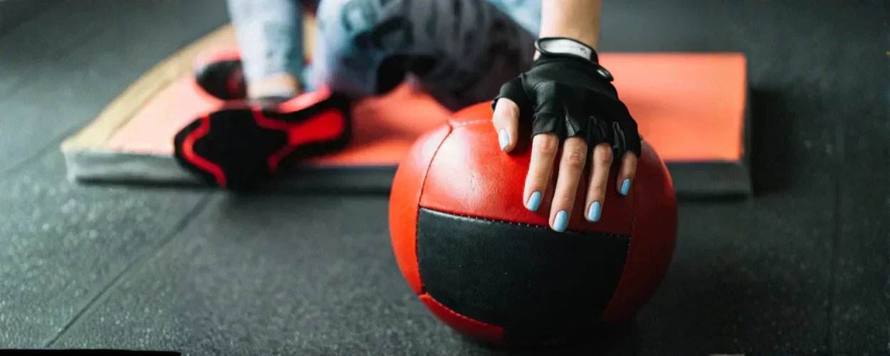  seseorang mengenakan sarung tangan gym saat berolahraga menggunakan medicine ball untuk melindungi telapak tangan dan meningkatkan grip saat latihan