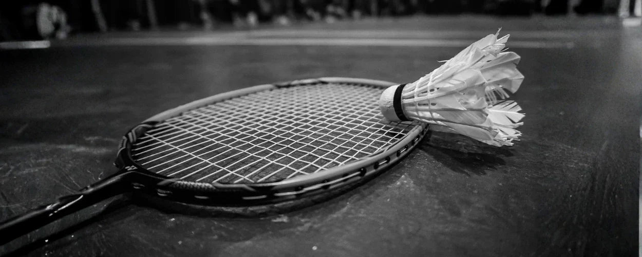 raket dan shuttlecock yang tergeletak di lapangan, menggambarkan semangat dan perjalanan panjang dalam sejarah bulu tangkis di Indonesia