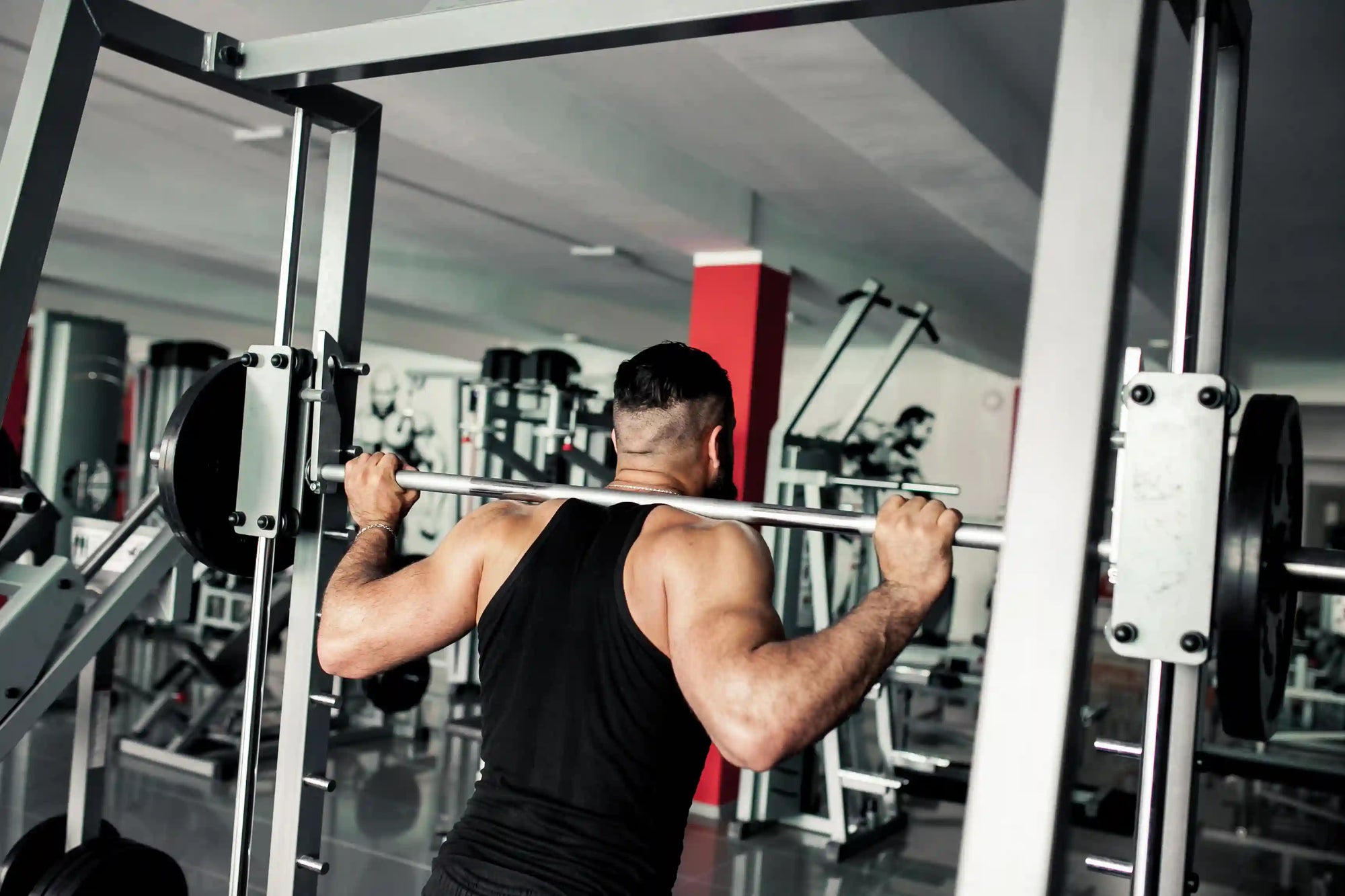 Seorang pria sedang berlatih menggunakan Smith Machine Shoulder Press di gym untuk membangun kekuatan bahu dan lengan