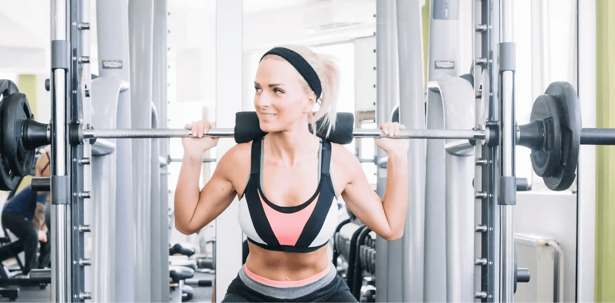 Seorang wanita sedang melakukan Smith Machine Squat di gym dengan posisi tubuh yang stabil untuk melatih kekuatan kaki dan glutes