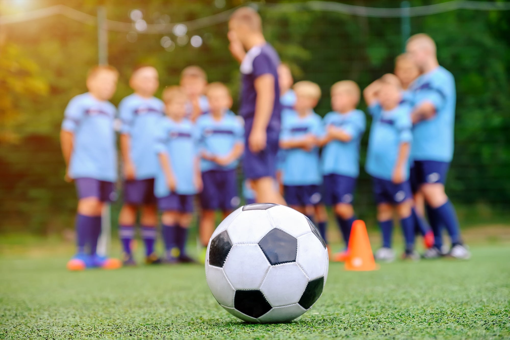 anak-anak berjersey biru berlatih bersama pelatih untuk belajar posisi pemain sepakbola.