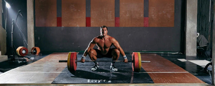 Seorang lifter bersiap melakukan sumo deadlift dari posisi awal dengan pinggul rendah dan torso lebih tegak di atas barbell.