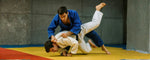 dua orang atlet sedang mempraktikkan teknik dasar judo dimana salah satunya sedang membanting lawannya