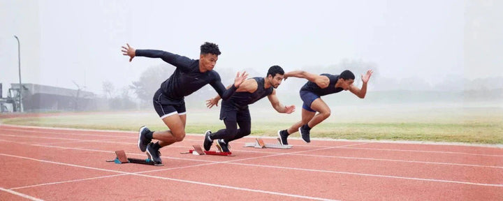 tiga pelari yang melakukan start pada lintasan atletik, masing-masing dalam posisi melesat maju, menggambarkan penerapan teknik dasar lari pendek seperti start eksplosif, akselerasi, dan dorongan kaki yang kuat