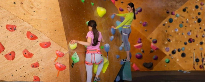 2 orang anak perempuan sedang mencoba teknik dasar wall climbing di area indoor