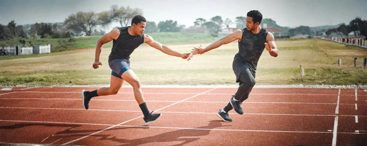 2 atlet lari estafet sedang dalam posisi penyerahan tongkat di lintasan atletik sebagai contoh teknik lari estafet yang benar