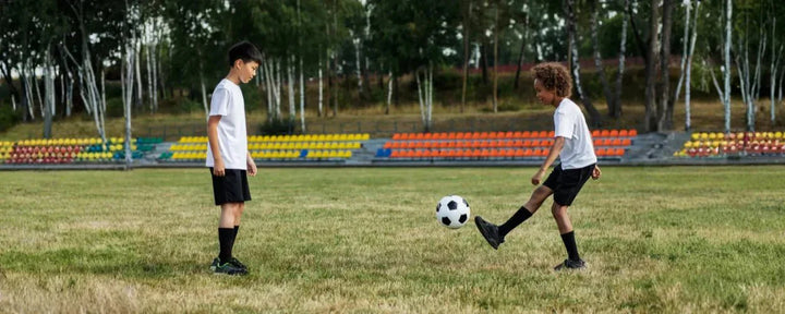 Dua anak sedang berlatih teknik passing sepak bola di lapangan dengan fokus untuk meningkatkan akurasi dan kerja sama tim