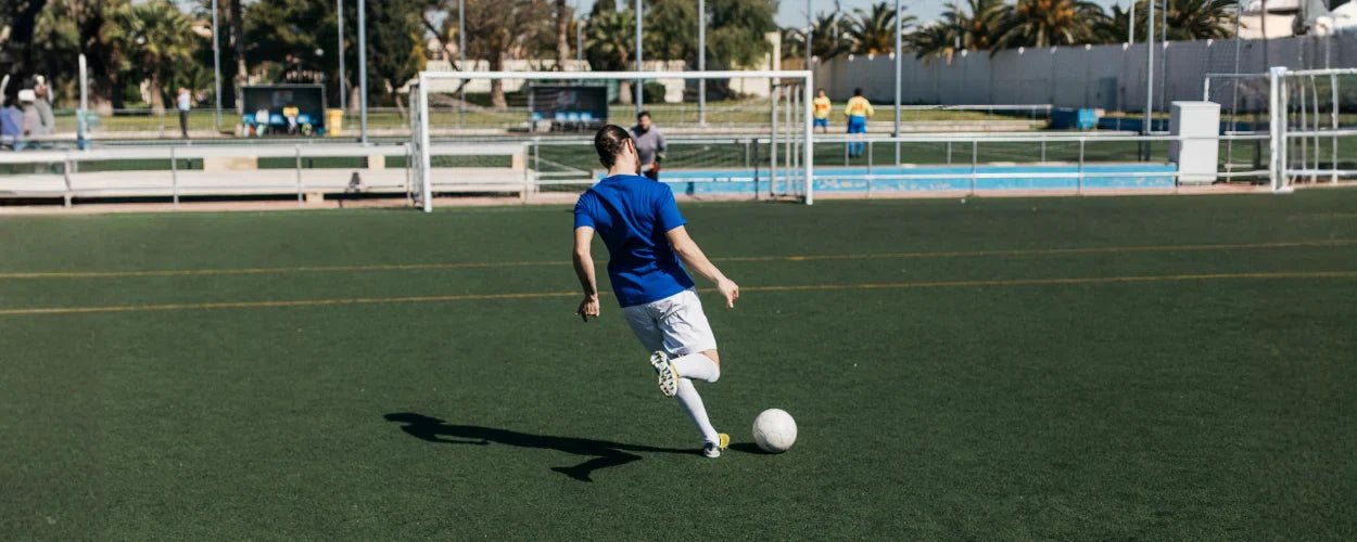 Seorang pria sedang mempraktikkan teknik menendang bola di lapangan rumput dengan fokus dan posisi tubuh yang seimbang