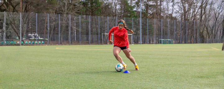 pemain sepak bola yang sedang mempraktikkan teknik menggiring bola dengan kontrol kaki yang baik saat bergerak di lapangan