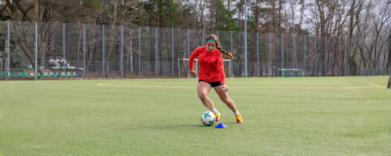 pemain sepak bola yang sedang mempraktikkan teknik menggiring bola dengan kontrol kaki yang baik saat bergerak di lapangan